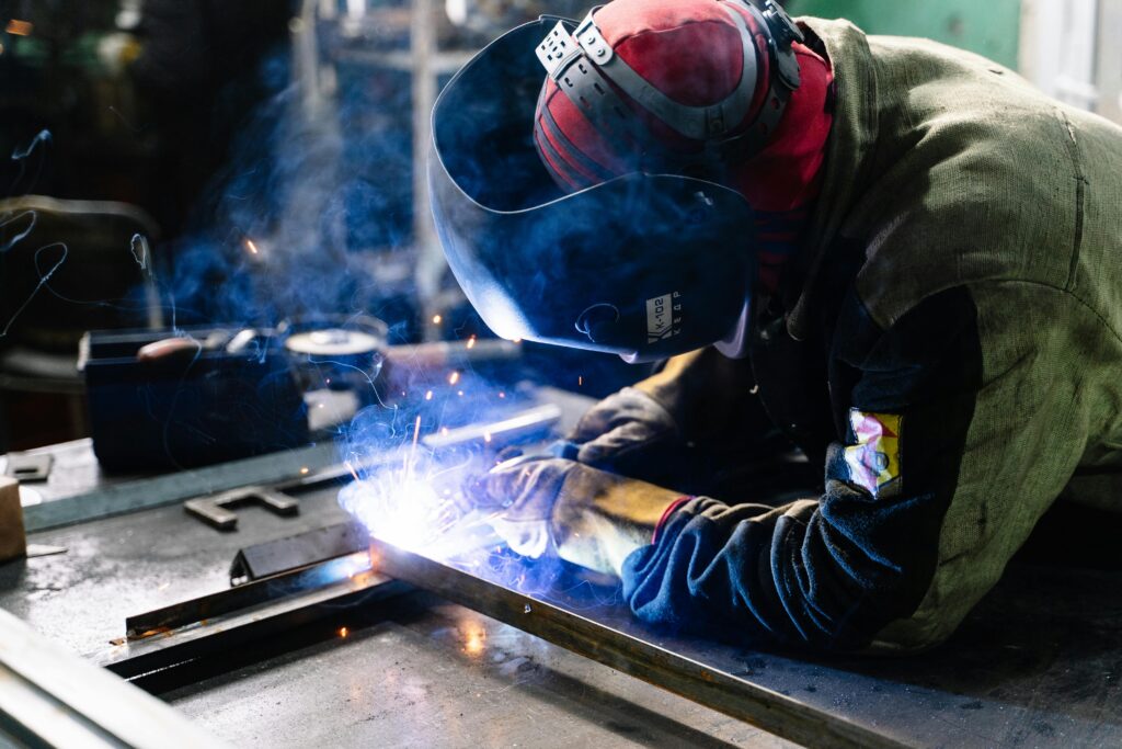 Bienvenido a A welder works on metal fabrication indoors, creating bright sparks and smoke.